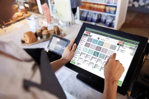 Kellnerin bedient an der Theke ein Kassensystem mit Touchscreen, auf dem die Gastronovi-Oberfläche mit Speisekarte, Menüpunkten und Bestellzettel zu sehen ist.