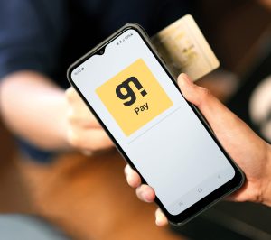 Person hält ein Smartphone in der Hand, auf dessen Display die Startseite der App Gastronovi Pay mit gelbem Logo zu sehen ist.